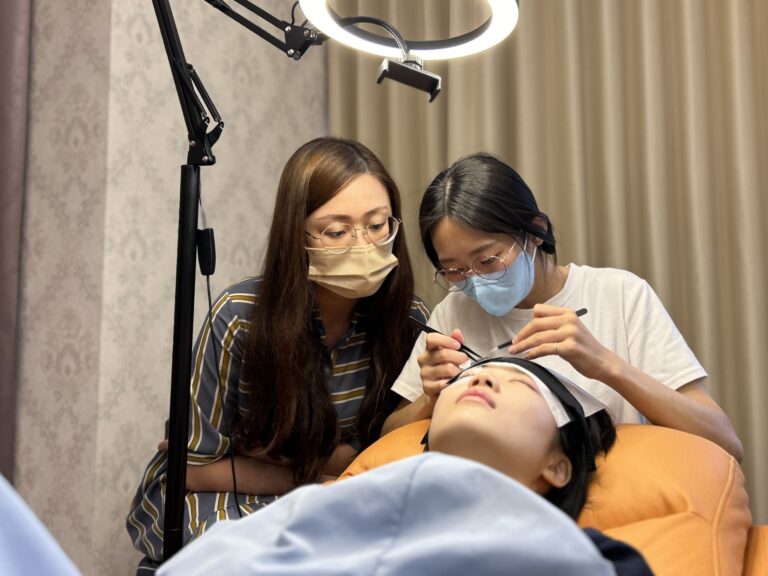 老師在環形燈下指導學員為真人模特兒接睫毛